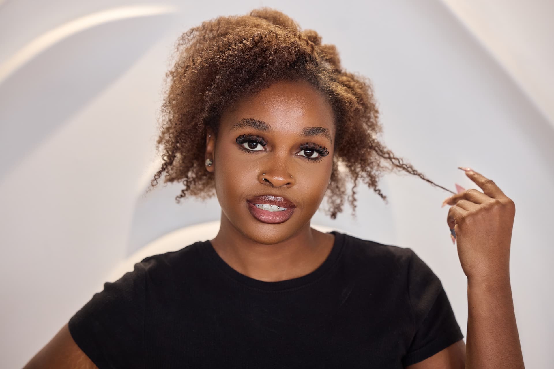 Portrait d'une personne touchant délicatement une mèche de ses cheveux frisés et volumineux aux reflets dorés, illustrant le soin et la mise en valeur des boucles naturelles.