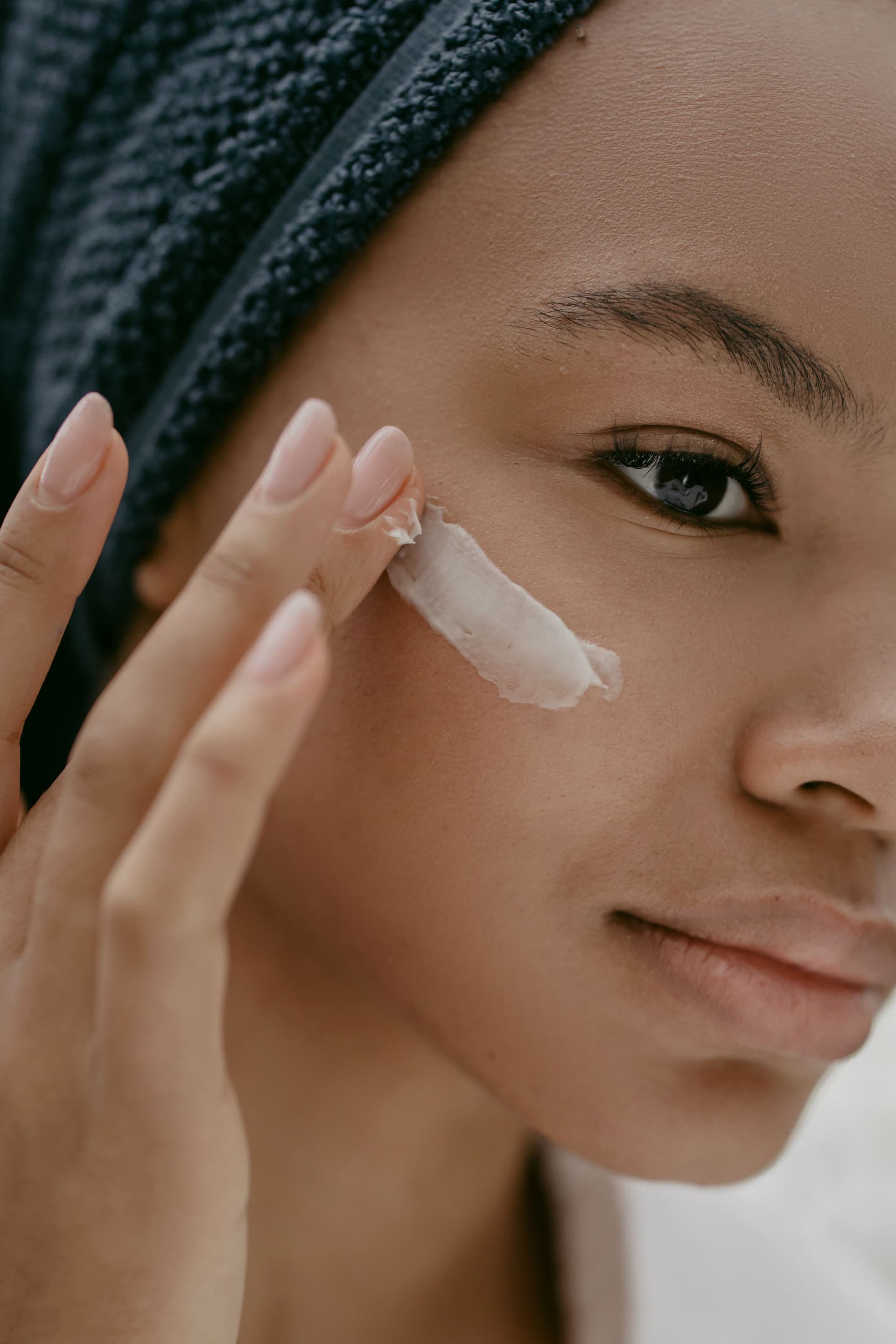 Gros plan sur une main appliquant avec douceur une touche de crème riche et hydratante sur la joue, lors d'un rituel de soin de la peau quotidien et attentif.
