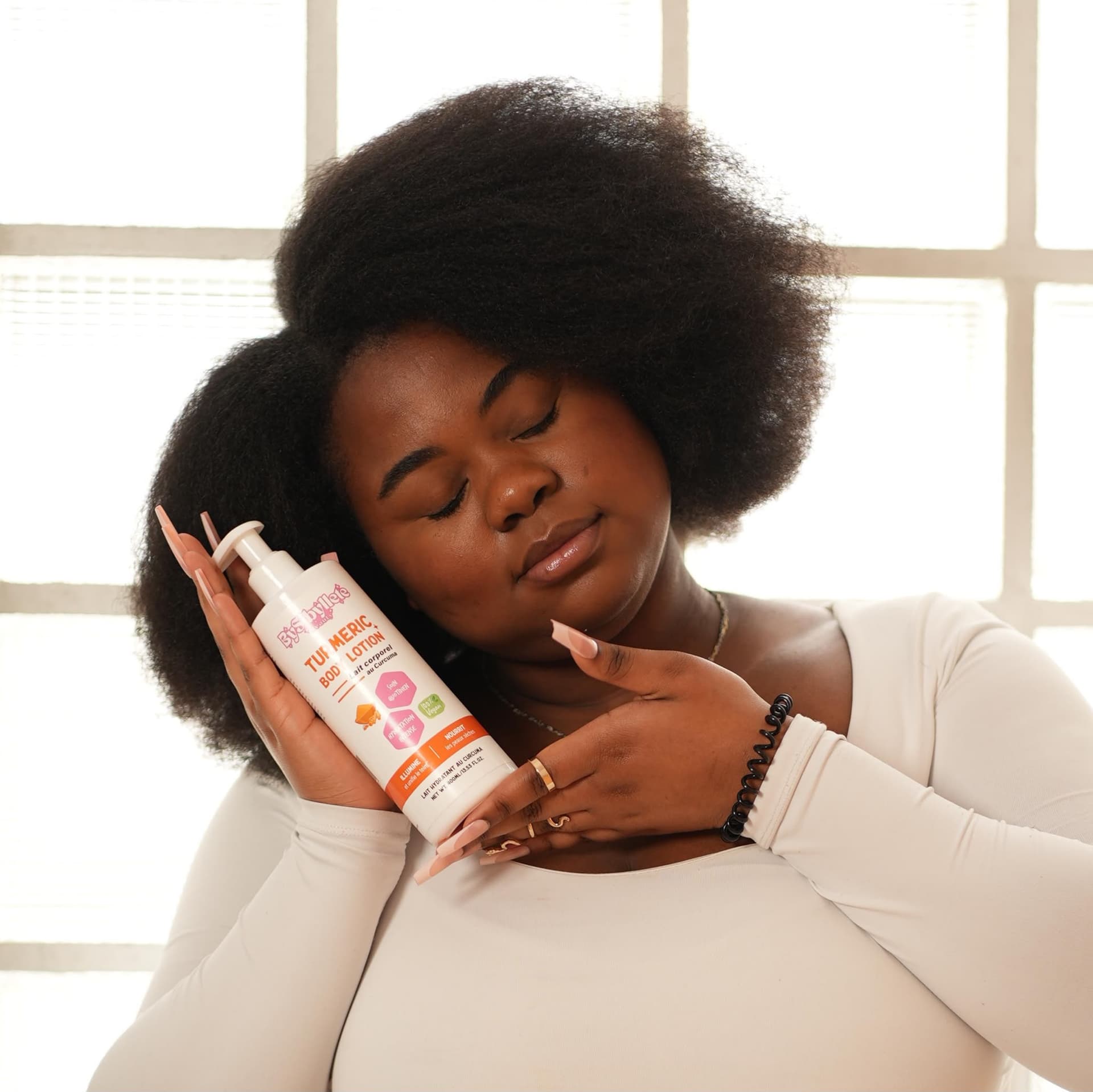 Une personne tenant le flacon de lait corporel au curcuma « Turmeric Body Lotion » de la marque BySyByllete.