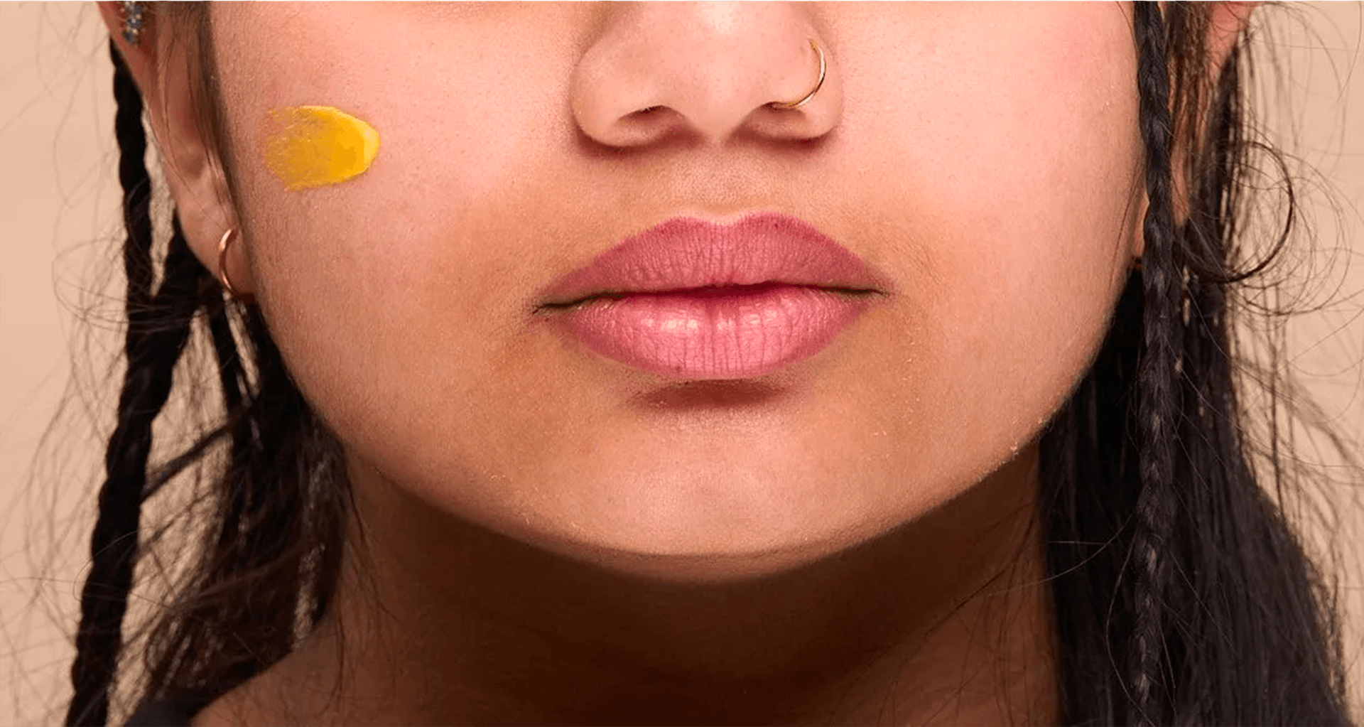 Très gros plan sur le bas du visage et les lèvres, montrant une touche de crème jaune au curcuma appliquée sur la joue, illustrant la texture du soin naturel.