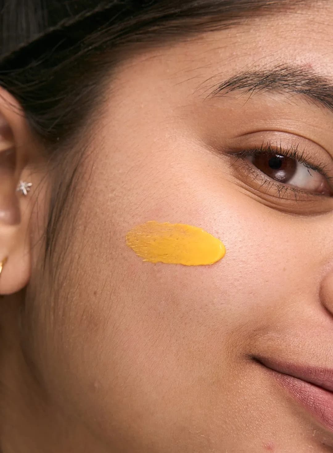 Très gros plan sur une touche de soin jaune au curcuma délicatement étalée sur la joue, à côté d'un léger sourire de profil.
