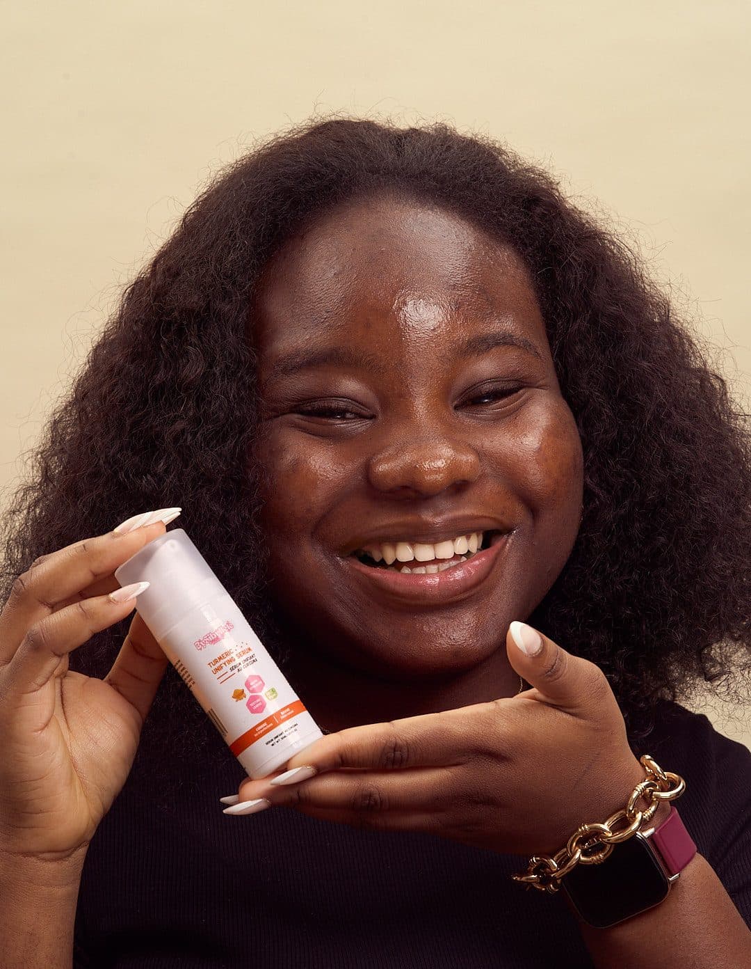 Jeune femme au teint éclatant et grand sourire montrant son produit skincare favori : le sérum unifiant au curcuma BySibyllete