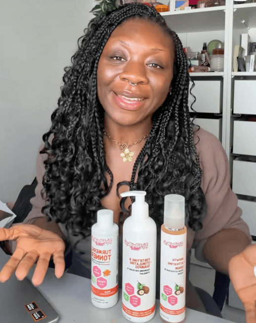 Femme souriante aux longues tresses présentant sa routine capillaire naturelle avec les shampoings et lotions BySibyllete