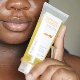 Personne présentant le tube de Nettoyant Visage au Curcuma et Aloe Vera (Turmeric Cleanser) By Sibyllete pour une routine de soin quotidienne.