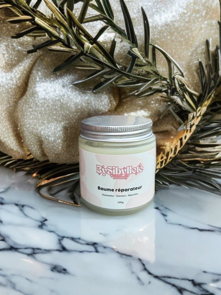 Baume réparateur 100g By Sibyllete posé sur du marbre, entouré de branches de romarin et de touches dorées.